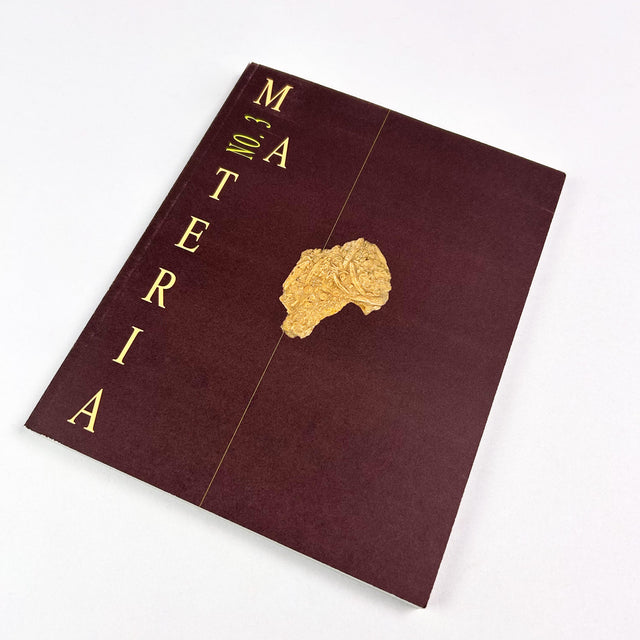 Maroon book titled 'Materia' with gold text and emblem on a white background